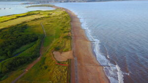 An aerial shot of Dawlish Warren with the sea to the right of the shot, the nature reserve to the left, the estuary mouth along the top and the dunes and beach running down the middle.