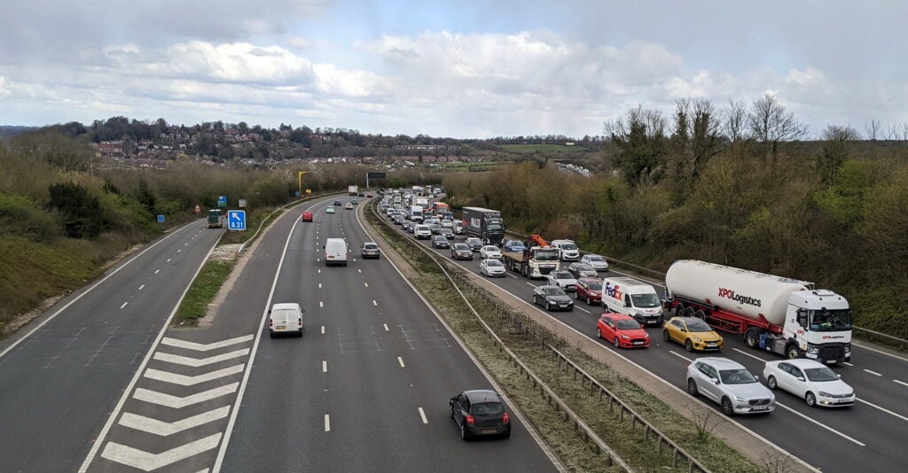 Motorway as seen from on top of a bridge. Heavy traffic is visible on one side and lighter traffic on the other.