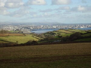 The city of Plymouth is seen in the distance with fields and an estuary in foreground.